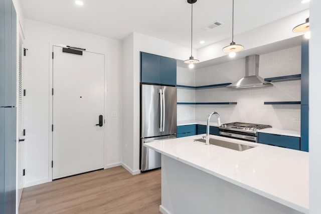 kitchen with wall chimney range hood, blue cabinetry, stainless steel appliances, and light countertops