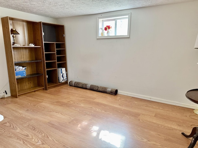 unfurnished room featuring light wood-style floors, a textured ceiling, and baseboards