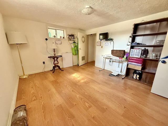 interior space with light wood-style floors, baseboards, visible vents, and a textured ceiling