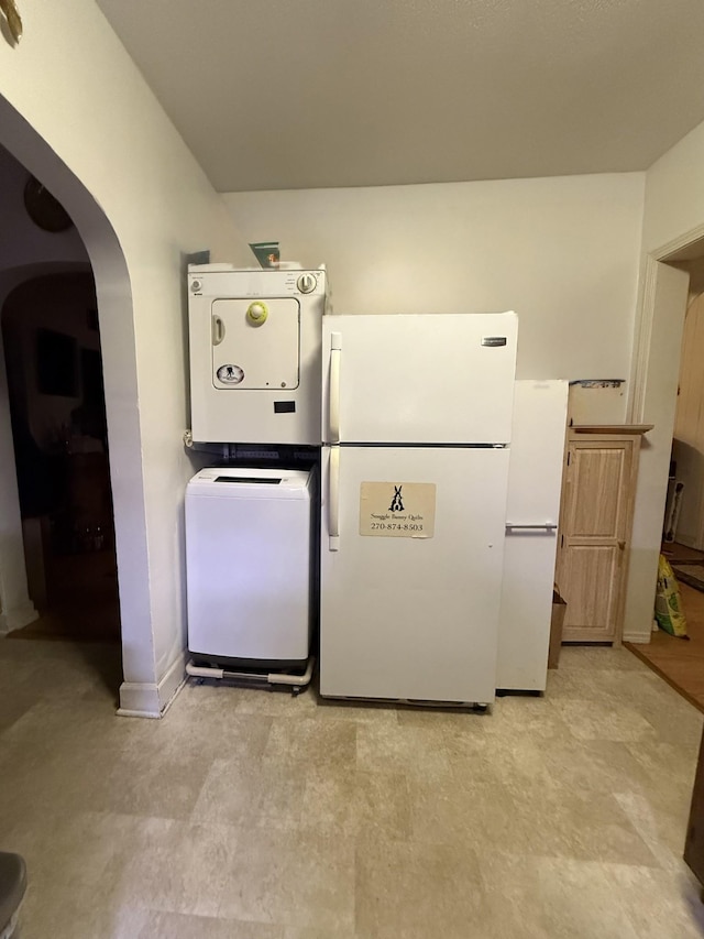 kitchen with stacked washer and dryer, freestanding refrigerator, arched walkways, and baseboards