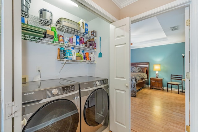 clothes washing area featuring visible vents, ornamental molding, washing machine and dryer, wood finished floors, and laundry area