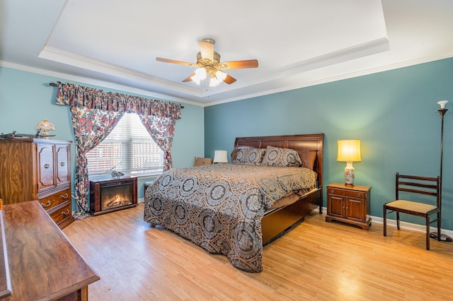 bedroom featuring light wood finished floors, a raised ceiling, ornamental molding, ceiling fan, and baseboards