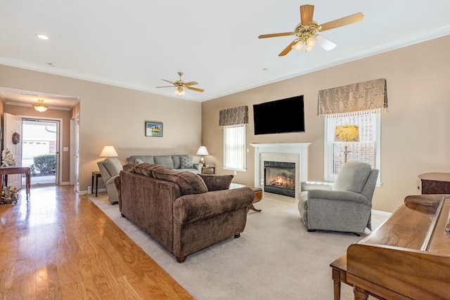 living room featuring light wood finished floors, ornamental molding, a glass covered fireplace, and baseboards