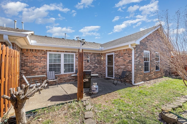 rear view of property with a patio, brick siding, a shingled roof, and fence