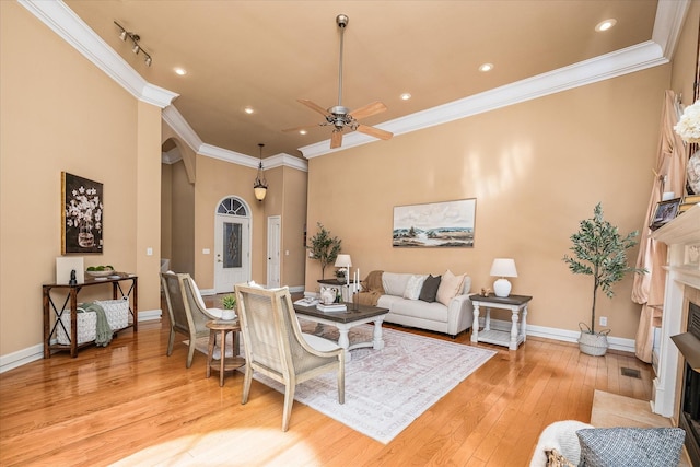 living area featuring arched walkways, a fireplace with flush hearth, baseboards, ornamental molding, and light wood-type flooring