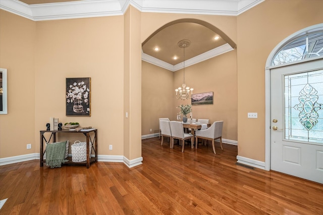 foyer entrance with ornamental molding, arched walkways, baseboards, and wood finished floors