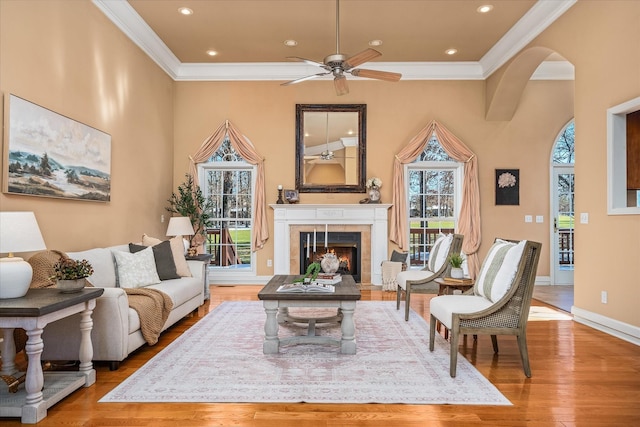 living area featuring a warm lit fireplace, arched walkways, wood finished floors, baseboards, and ornamental molding