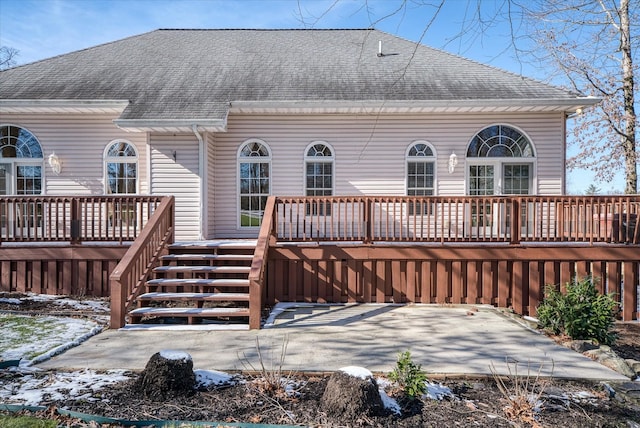 snow covered rear of property with roof with shingles, a patio, a wooden deck, and stairs