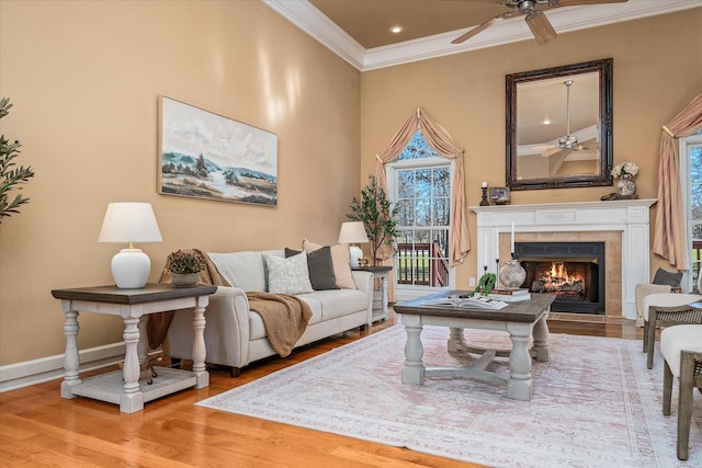 living room featuring ornamental molding, a tile fireplace, a ceiling fan, and wood finished floors