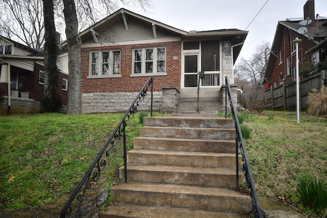 bungalow-style house with stairs, brick siding, a front yard, and a sunroom