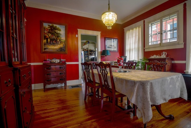 dining space featuring baseboards, visible vents, wood finished floors, crown molding, and a chandelier