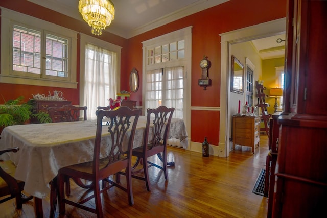 dining space with baseboards, a notable chandelier, ornamental molding, and wood finished floors