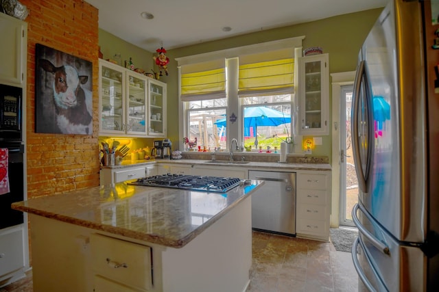 kitchen with stainless steel appliances, a sink, a kitchen island, white cabinets, and glass insert cabinets