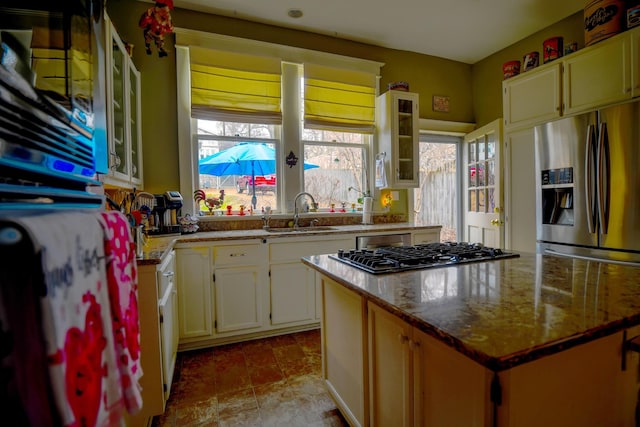 kitchen with appliances with stainless steel finishes, glass insert cabinets, a center island, light stone countertops, and a sink