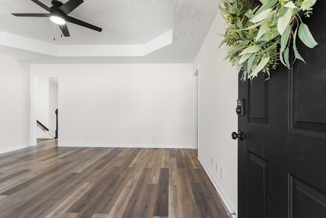 spare room featuring dark wood-style flooring, a raised ceiling, ceiling fan, a textured ceiling, and baseboards