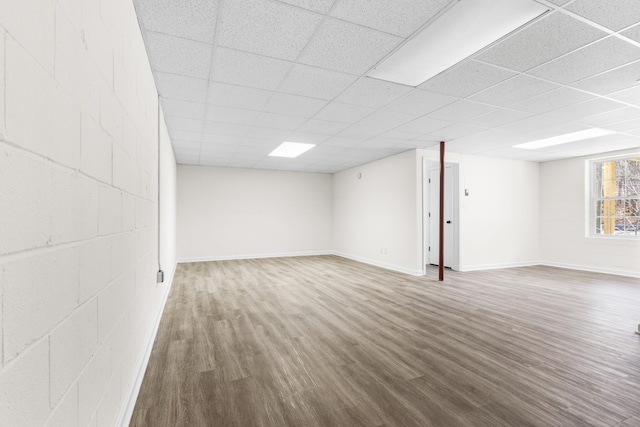 below grade area with concrete block wall, a drop ceiling, baseboards, and wood finished floors