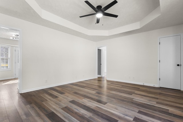 spare room with dark wood-type flooring, a raised ceiling, a textured ceiling, and baseboards