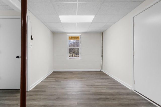 below grade area with a drop ceiling, baseboards, and wood finished floors