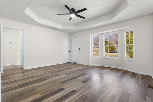 empty room featuring a textured ceiling, dark wood-style flooring, a ceiling fan, baseboards, and a tray ceiling