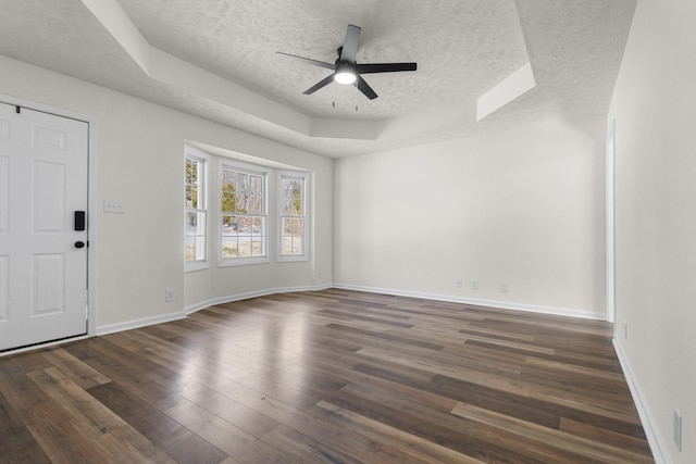 interior space with a textured ceiling, a ceiling fan, baseboards, a tray ceiling, and dark wood finished floors