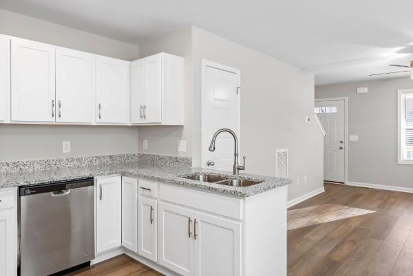 kitchen featuring light stone counters, white cabinets, dishwasher, and a sink