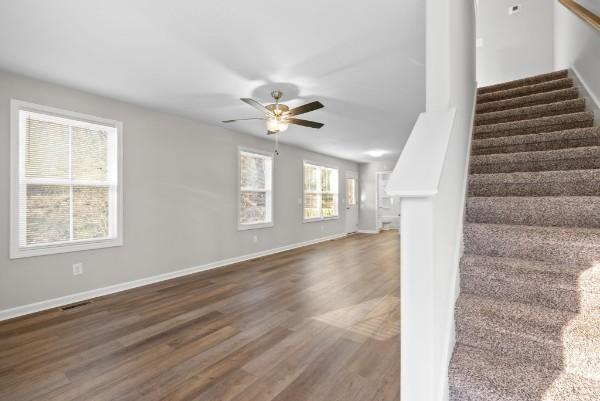 unfurnished living room with ceiling fan, stairs, baseboards, and dark wood finished floors