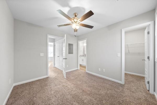 unfurnished bedroom featuring light carpet, baseboards, ceiling fan, a spacious closet, and a closet