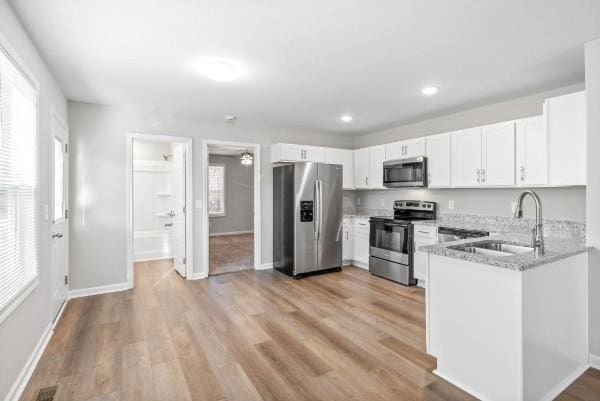 kitchen featuring light stone counters, a sink, white cabinetry, appliances with stainless steel finishes, and light wood finished floors