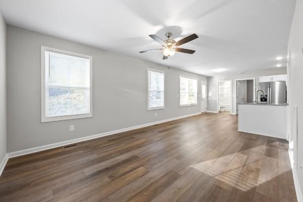 unfurnished living room featuring dark wood-style flooring, a ceiling fan, and baseboards