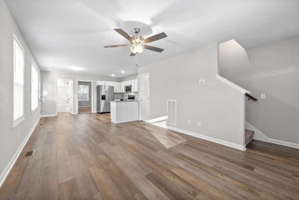 unfurnished living room featuring wood finished floors, a ceiling fan, visible vents, baseboards, and stairway