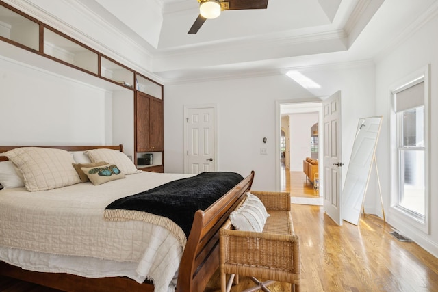 bedroom featuring visible vents, a towering ceiling, ornamental molding, wood finished floors, and a tray ceiling