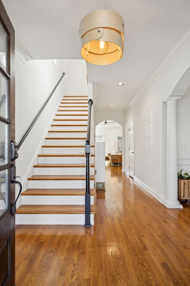 foyer entrance featuring arched walkways, stairway, wood finished floors, crown molding, and ornate columns