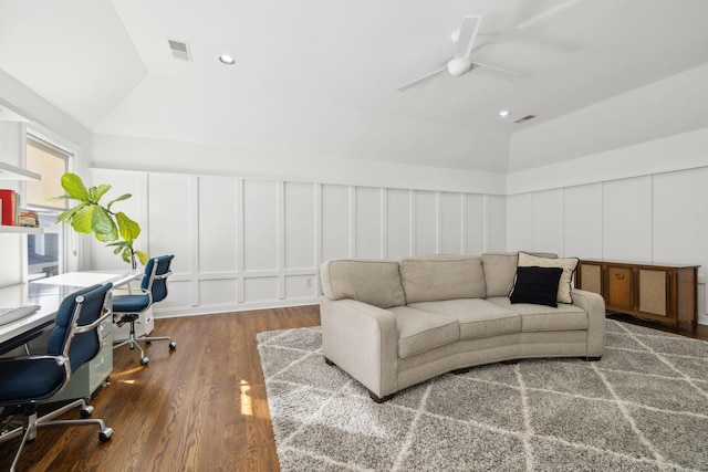 living area with vaulted ceiling, wood finished floors, a ceiling fan, and a decorative wall