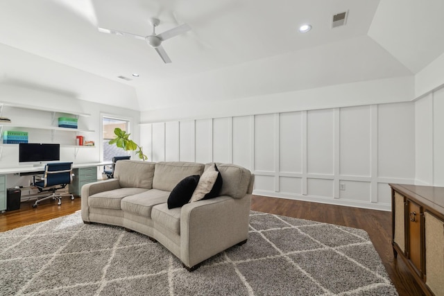 living area with lofted ceiling, ceiling fan, a decorative wall, dark wood-type flooring, and visible vents