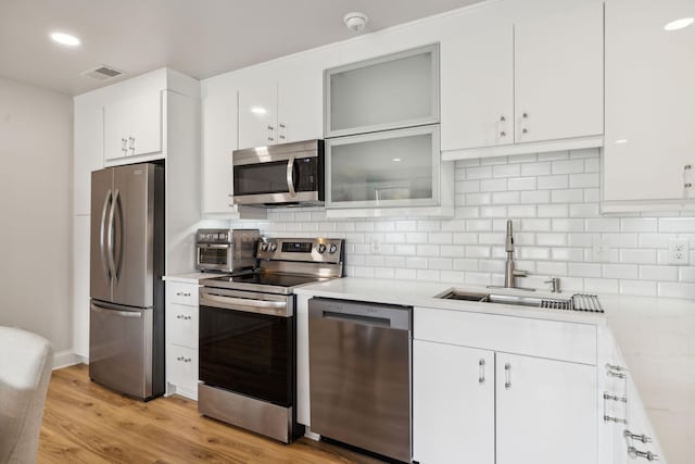 kitchen with tasteful backsplash, appliances with stainless steel finishes, light wood-style floors, white cabinetry, and a sink