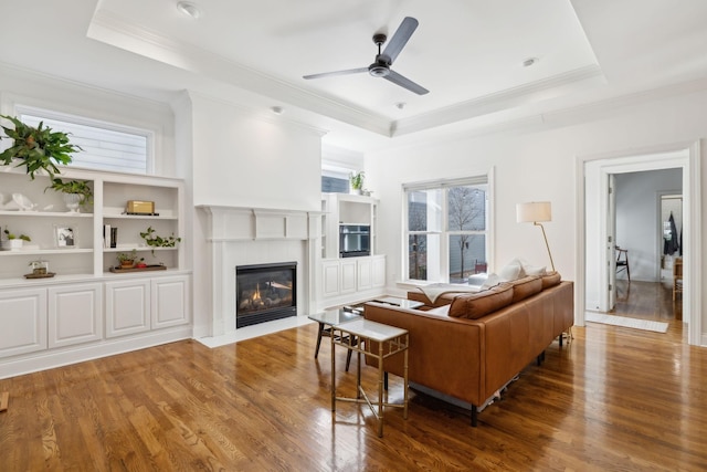 living area featuring a fireplace with flush hearth, a tray ceiling, and wood finished floors