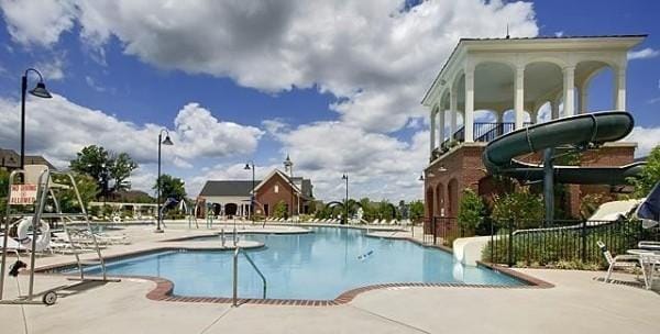 community pool featuring a patio area, fence, and a water slide