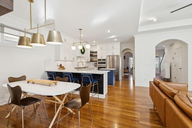 dining room featuring arched walkways, recessed lighting, light wood-style flooring, ornamental molding, and baseboards