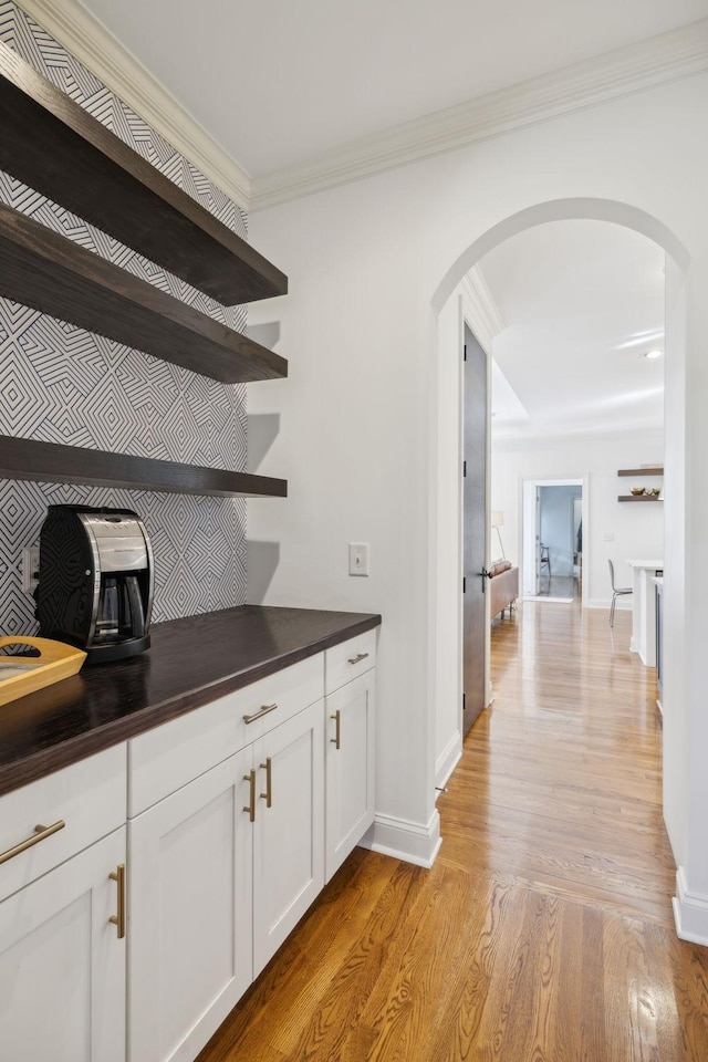 bar with arched walkways, crown molding, light wood-style flooring, and baseboards