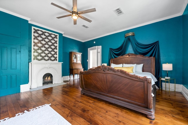 bedroom featuring wood finished floors, visible vents, baseboards, a lit fireplace, and ornamental molding