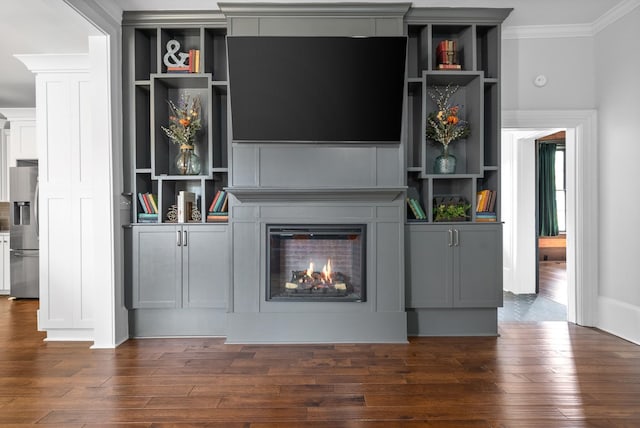 unfurnished living room with a warm lit fireplace, built in shelves, ornamental molding, and dark wood-style flooring