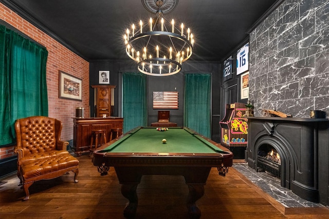 game room with ornamental molding, brick wall, wood finished floors, a warm lit fireplace, and billiards