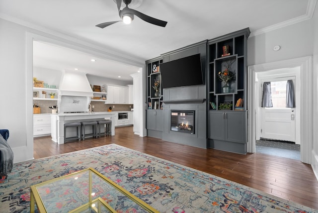 living room with crown molding, dark wood finished floors, recessed lighting, a ceiling fan, and a multi sided fireplace