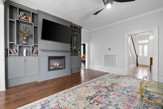 living area featuring ceiling fan, dark wood-style flooring, visible vents, a lit fireplace, and crown molding