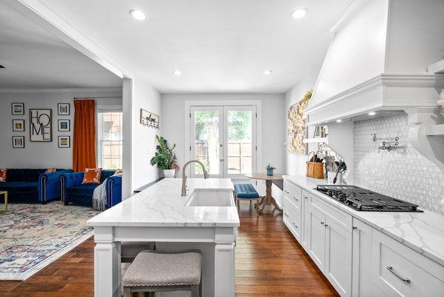 kitchen with a breakfast bar area, a sink, gas cooktop, light stone countertops, and premium range hood