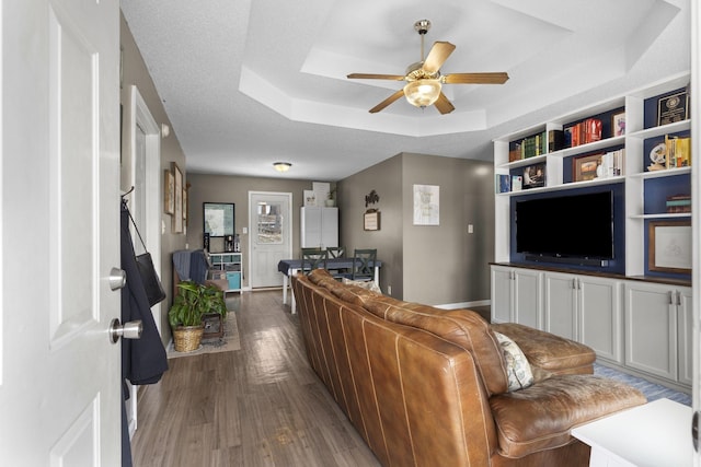 living room with a tray ceiling, a ceiling fan, a textured ceiling, wood finished floors, and baseboards