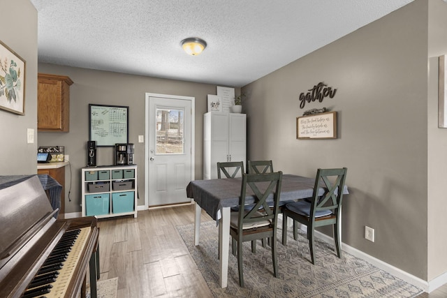 dining room featuring light wood-type flooring, baseboards, and a textured ceiling