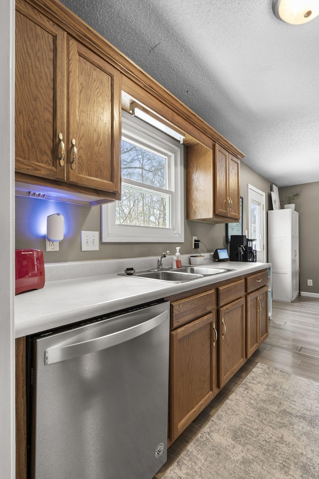 kitchen featuring light countertops, light wood-style flooring, stainless steel dishwasher, brown cabinetry, and a sink