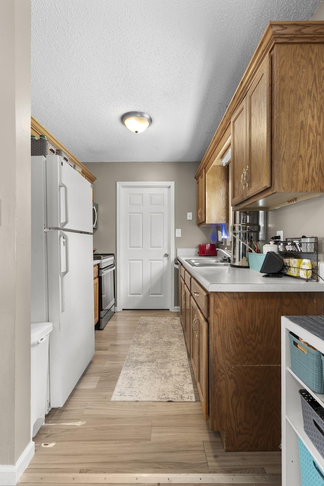 kitchen with light wood-style flooring, brown cabinets, stainless steel appliances, light countertops, and a sink