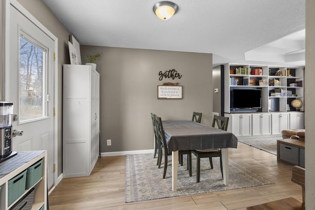 dining space featuring light wood-style flooring, baseboards, and a textured ceiling